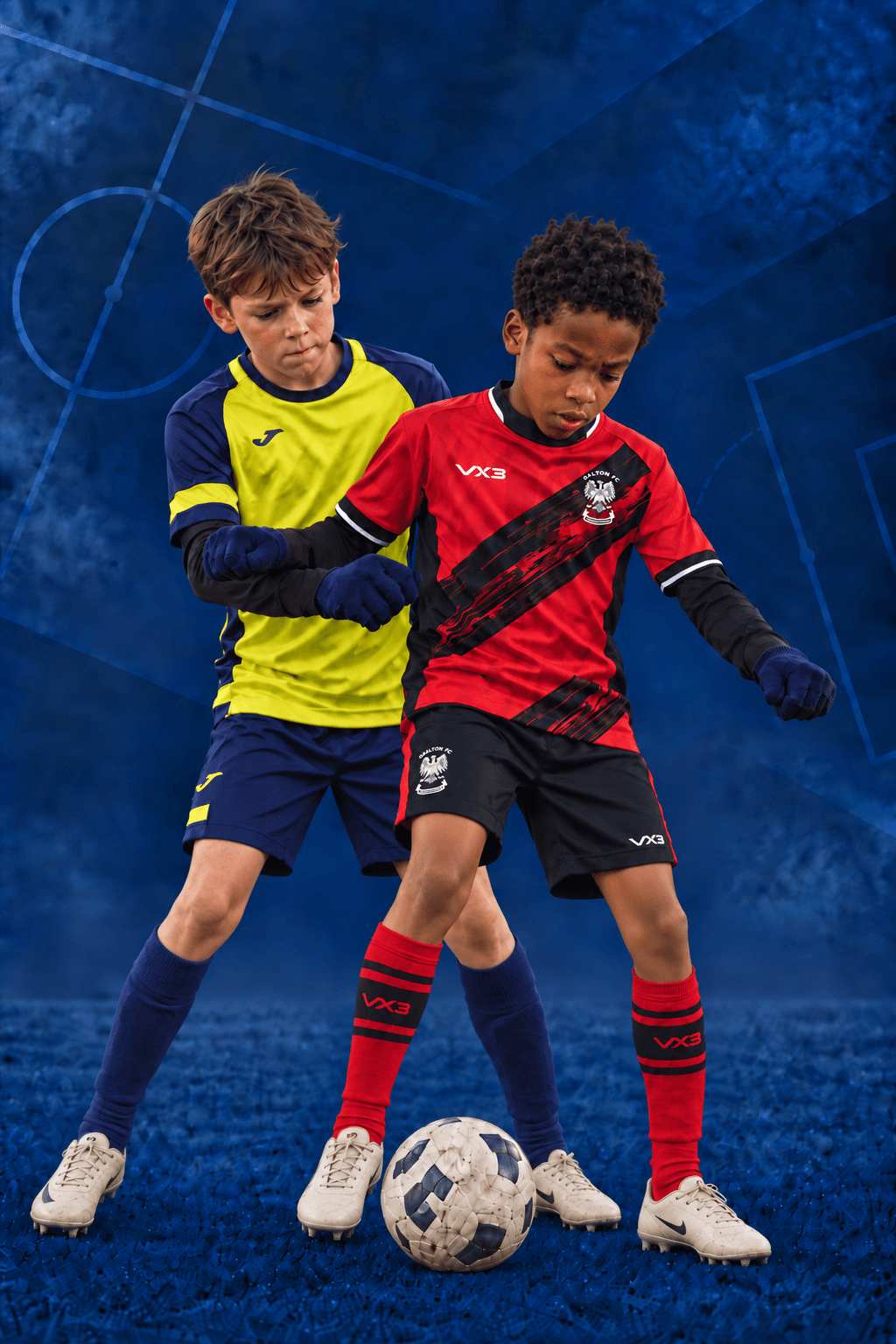 Two young footballers competing for the ball, one in red and black, the other in yellow and navy