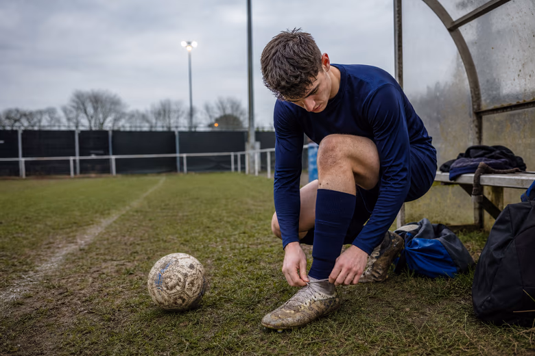 Adult player preparing for training with a football on a community pitch